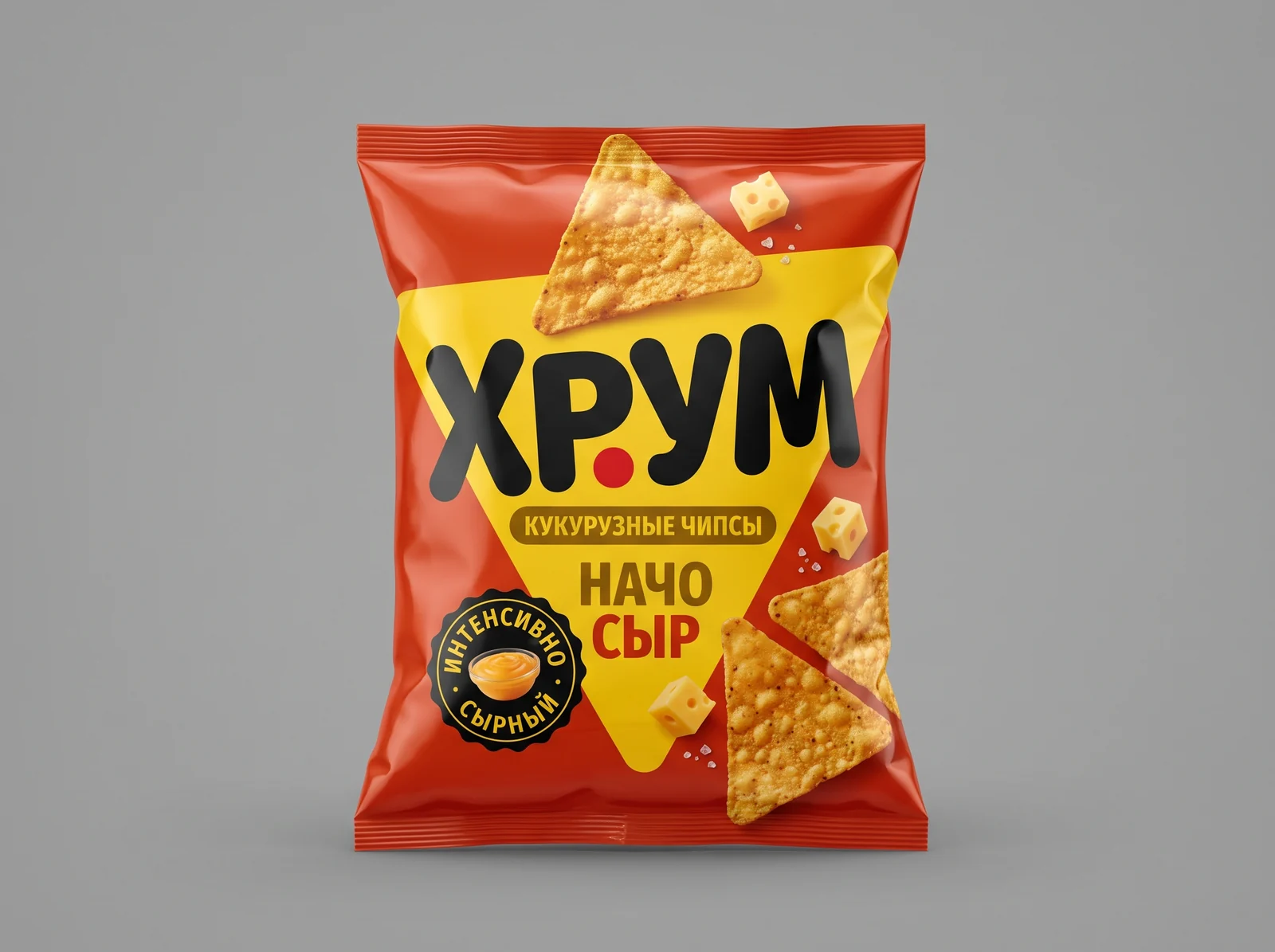 Красная глянцевая пачка кукурузных чипсов на сером фоне: жёлтый треугольник, название «Хрум» жирными чёрными буквами, надписи «Кукурузные чипсы» и «Начо сыр», круглая чёрная печать, треугольные чипсы и кубики сыра